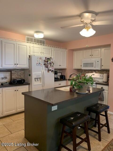 325 Rosewood Dr, Louisville, KY 40223 - kitchen with white appliances, dark countertops, a breakfast bar, and light tile patterned flooring