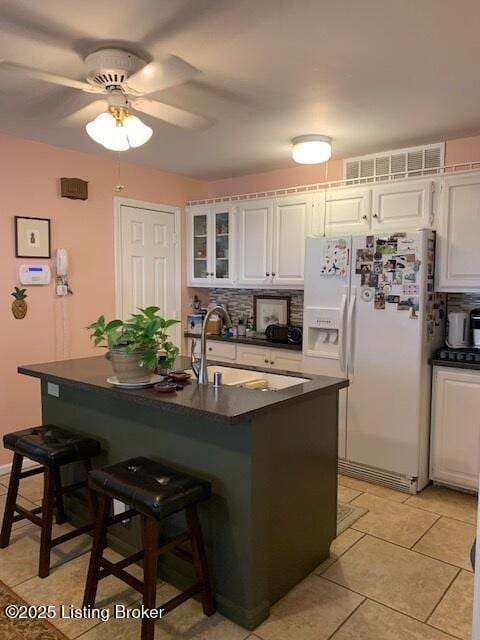 325 Rosewood Dr, Louisville, KY 40223 - kitchen featuring white refrigerator with ice dispenser, dark countertops, a kitchen breakfast bar, white cabinets, and decorative backsplash