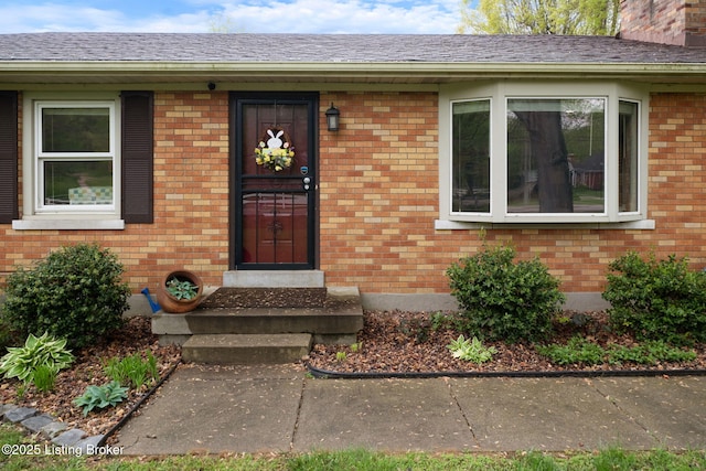 entrance to property with brick siding and a shingled roof
