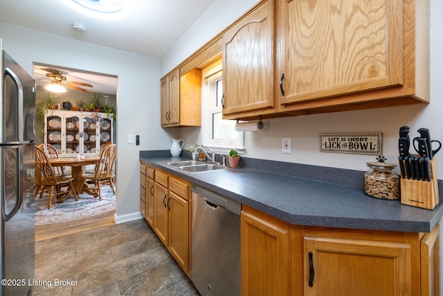 kitchen featuring dark countertops, stainless steel dishwasher, a sink, freestanding refrigerator, and ceiling fan