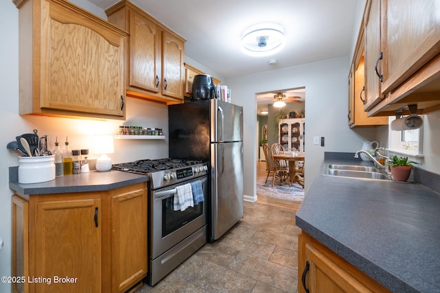 kitchen featuring stainless steel appliances, stone finish floor, dark countertops, a sink, and ceiling fan