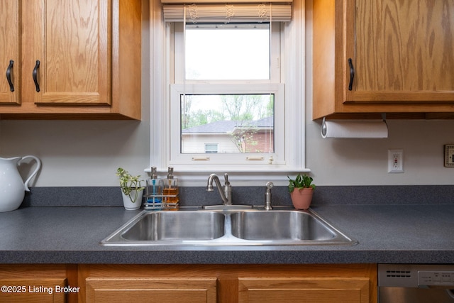 kitchen with brown cabinets, stainless steel dishwasher, dark countertops, and a sink