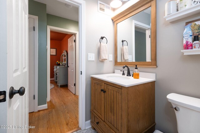 half bath featuring visible vents, wood finished floors, vanity, and toilet