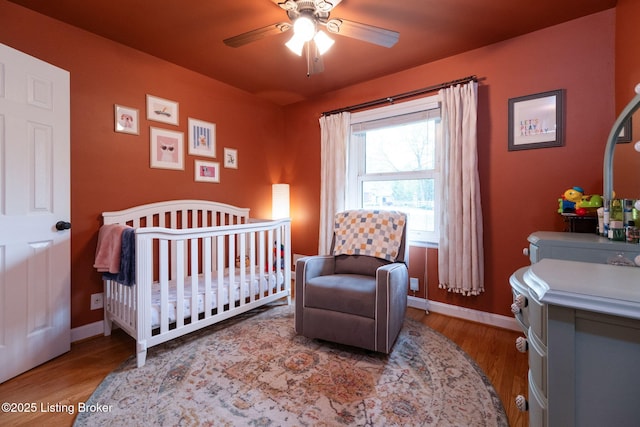 bedroom with a nursery area, baseboards, and wood finished floors