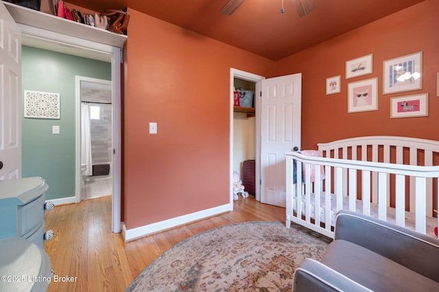 bedroom featuring light wood-style flooring, baseboards, a closet, ceiling fan, and a nursery area