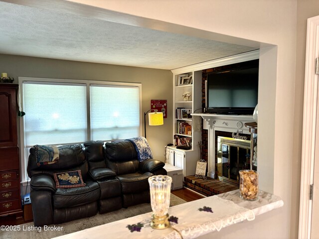 living room with built in features, wood finished floors, a textured ceiling, and a fireplace