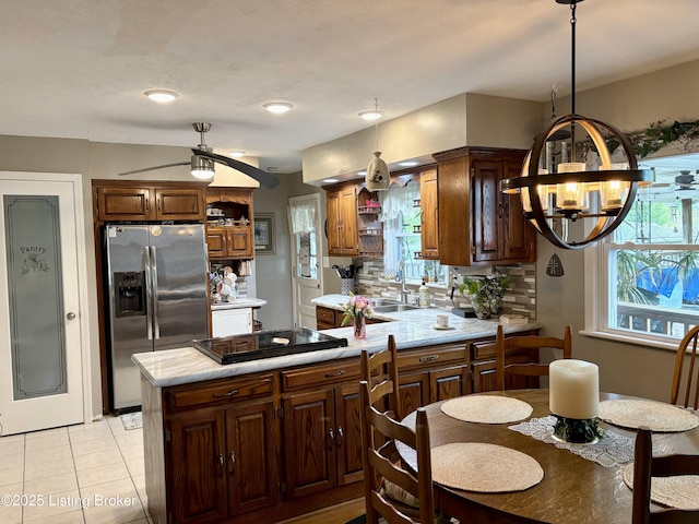 kitchen with a sink, an inviting chandelier, decorative backsplash, stainless steel refrigerator with ice dispenser, and cooktop