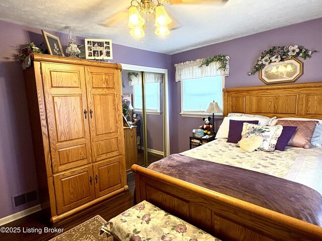 bedroom featuring dark wood-style floors, visible vents, baseboards, a closet, and ceiling fan