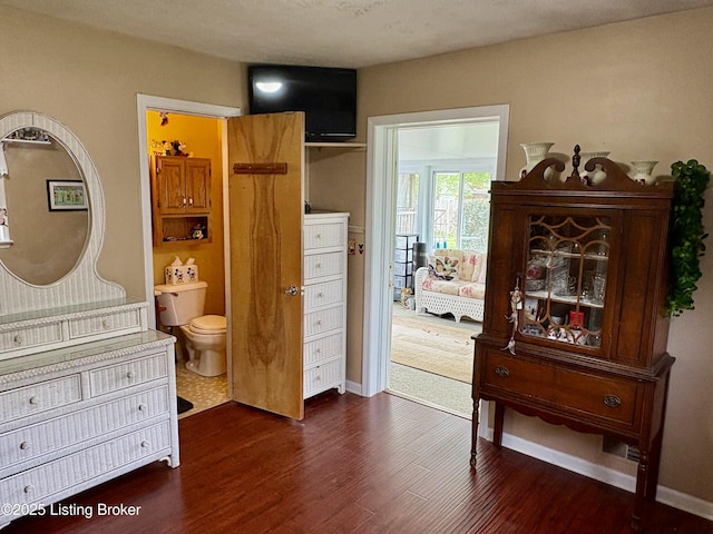 bedroom with dark wood-type flooring, ensuite bath, and baseboards