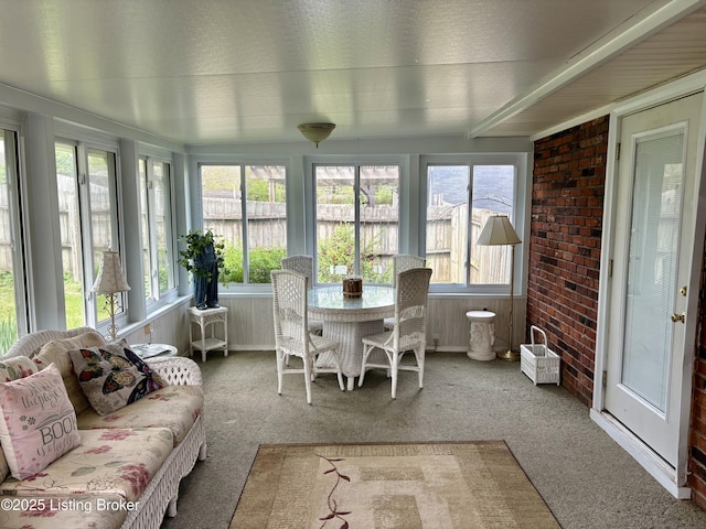 sunroom / solarium featuring brick wall, carpet floors, and a healthy amount of sunlight