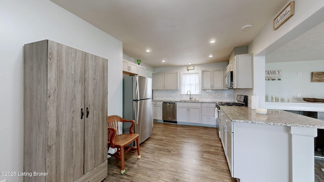 702 11th St, Carrollton, KY 41008 - kitchen featuring light stone counters, stainless steel appliances, backsplash, a sink, and light wood-style flooring