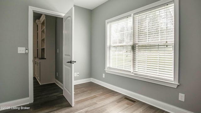 unfurnished room with baseboards, a healthy amount of sunlight, wood finished floors, and visible vents