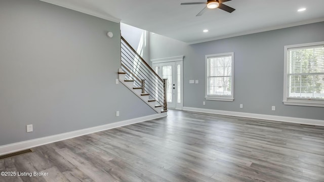 unfurnished living room featuring a ceiling fan, stairs, visible vents, and plenty of natural light