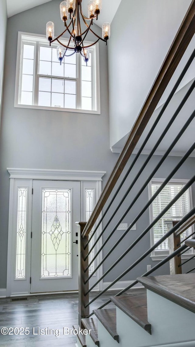 foyer entrance featuring high vaulted ceiling, stairway, wood finished floors, an inviting chandelier, and visible vents
