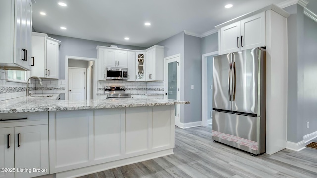 kitchen with tasteful backsplash, a sink, baseboards, a peninsula, and appliances with stainless steel finishes