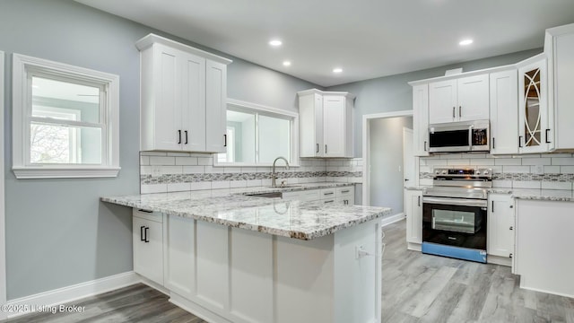 kitchen featuring decorative backsplash, white cabinetry, light wood-style flooring, a peninsula, and appliances with stainless steel finishes