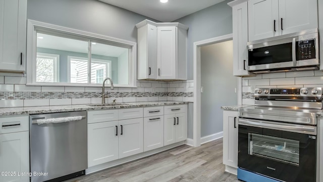kitchen with a sink, decorative backsplash, light wood-style floors, stainless steel appliances, and white cabinets
