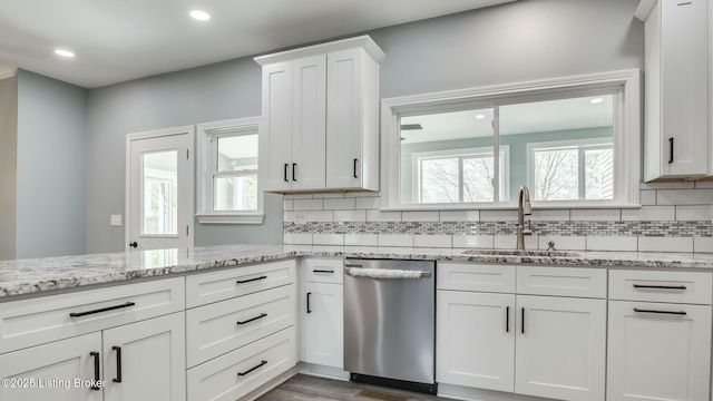 kitchen with stainless steel dishwasher, a sink, plenty of natural light, backsplash, and white cabinetry