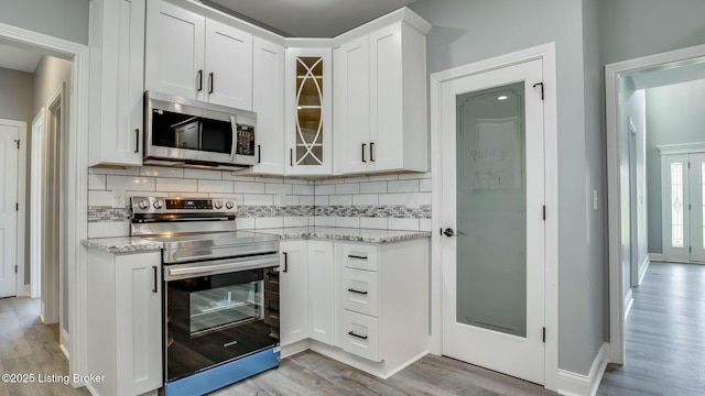 kitchen featuring white cabinets, stainless steel appliances, light wood-type flooring, backsplash, and light stone counters