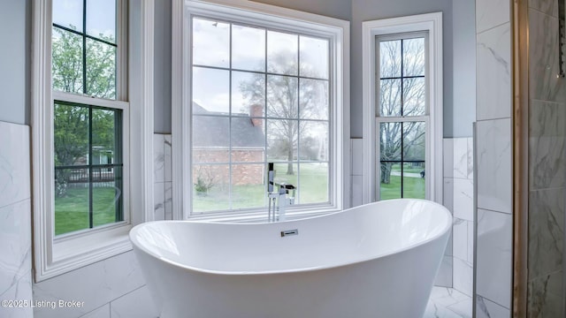 bathroom with a freestanding tub, marble finish floor, and a wealth of natural light