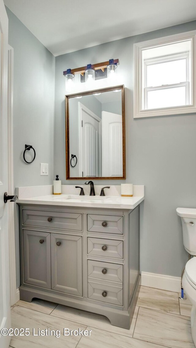 half bathroom with baseboards, vanity, and toilet