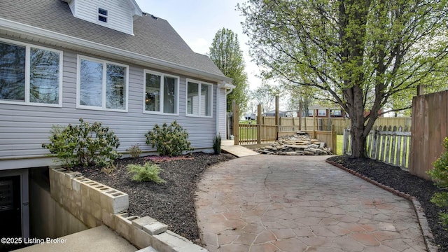 view of side of home with a patio area, roof with shingles, and fence