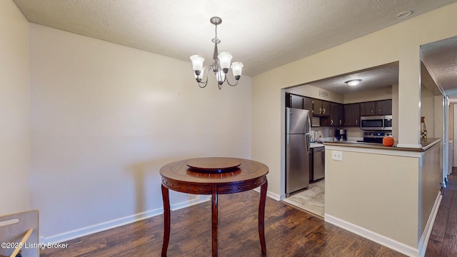 kitchen with stainless steel appliances, dark brown cabinetry, an inviting chandelier, and wood finished floors