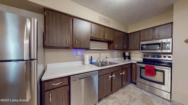 kitchen with a textured ceiling, dark brown cabinets, light countertops, a sink, and stainless steel appliances