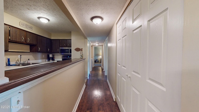corridor featuring a textured ceiling, baseboards, a sink, and dark wood-style floors