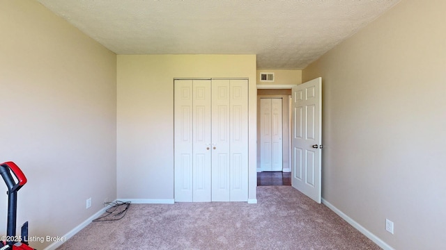 unfurnished bedroom with visible vents, baseboards, a closet, a textured ceiling, and carpet flooring