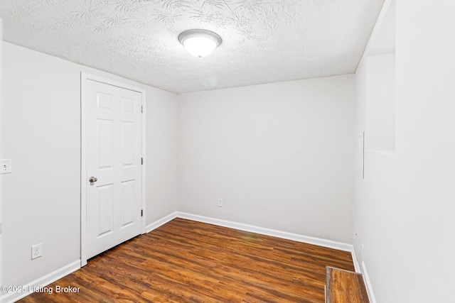 spare room featuring baseboards, a textured ceiling, and dark wood-type flooring