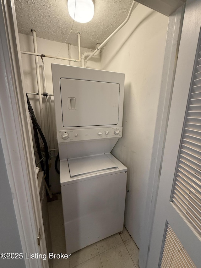 laundry area featuring a textured ceiling and stacked washer / drying machine