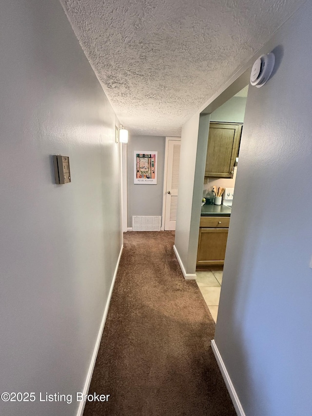 hallway with a textured ceiling, light colored carpet, baseboards, and visible vents