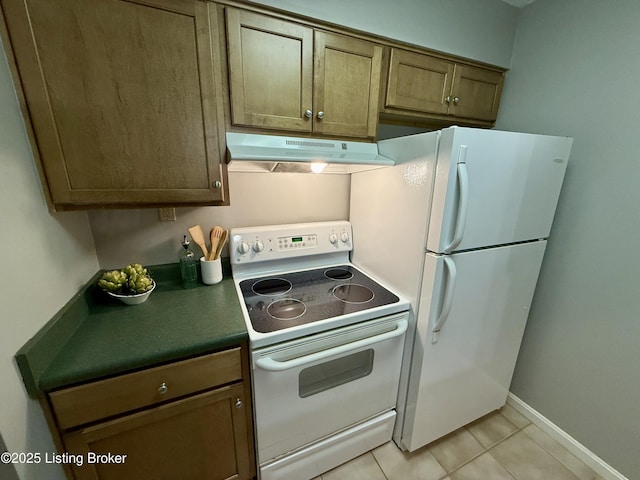 kitchen featuring white appliances, light tile patterned flooring, dark countertops, and under cabinet range hood