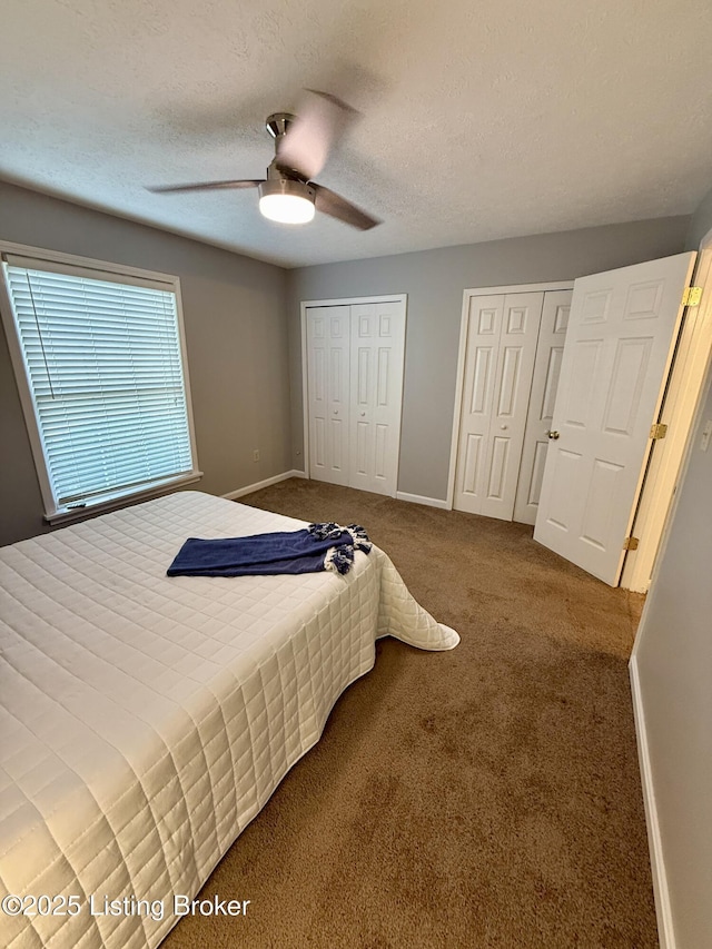 bedroom featuring two closets, baseboards, ceiling fan, a textured ceiling, and carpet