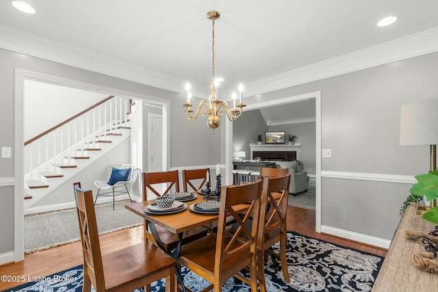 dining space with an inviting chandelier, stairway, a fireplace, crown molding, and wood finished floors