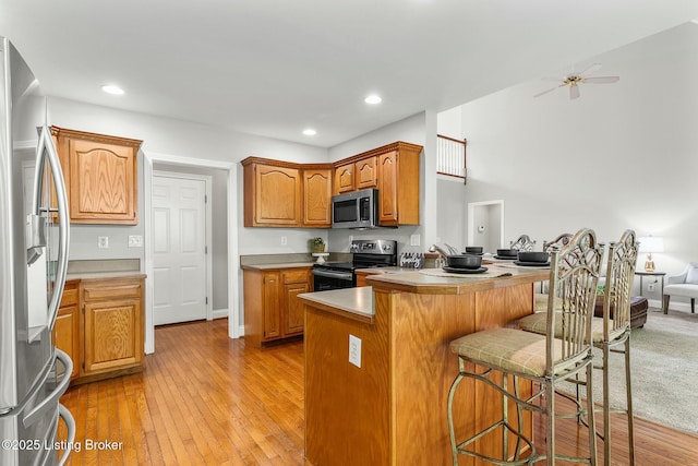 kitchen with light wood-style flooring, appliances with stainless steel finishes, a breakfast bar, light countertops, and a peninsula