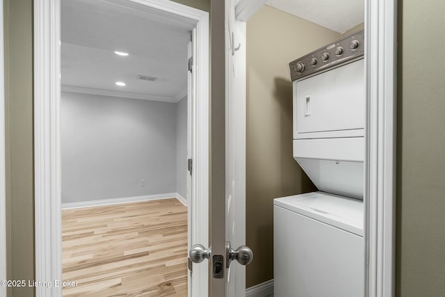 laundry area with light wood finished floors, stacked washer and clothes dryer, crown molding, visible vents, and baseboards