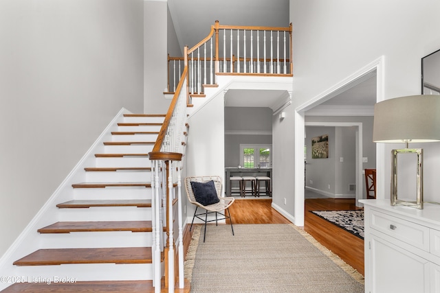 stairs featuring baseboards, wood finished floors, ornamental molding, and a towering ceiling