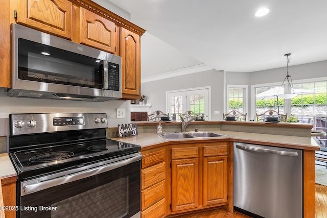 kitchen with crown molding, a sink, stainless steel appliances, a peninsula, and brown cabinetry