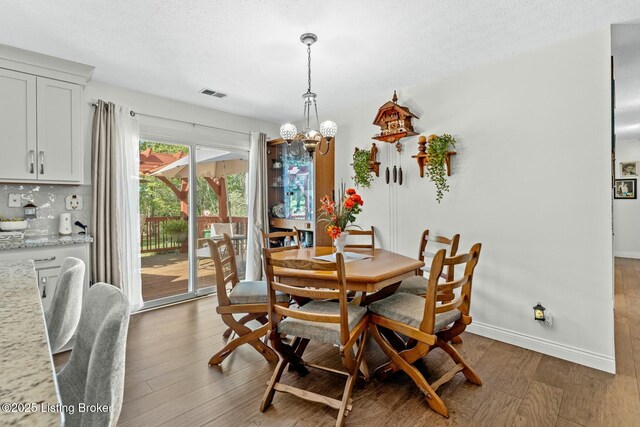 dining area featuring wood finished floors, visible vents, a chandelier, and a textured ceiling