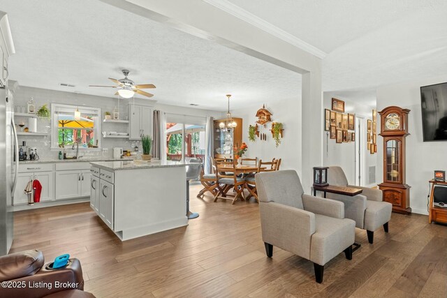 living area featuring visible vents, light wood-style floors, ornamental molding, and ceiling fan with notable chandelier