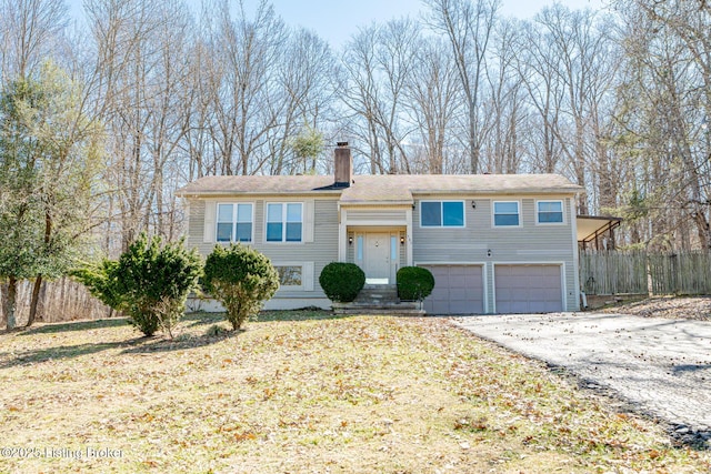 bi-level home featuring a chimney, fence, driveway, and a garage
