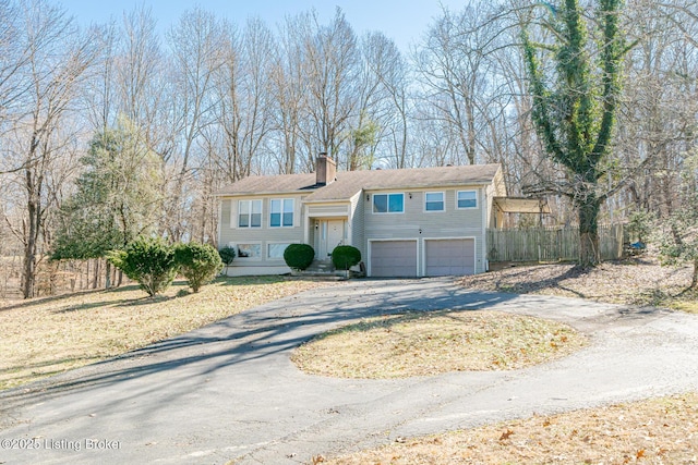 bi-level home with a garage, a chimney, aphalt driveway, and fence