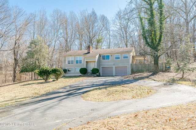 raised ranch with an attached garage, a chimney, aphalt driveway, and fence