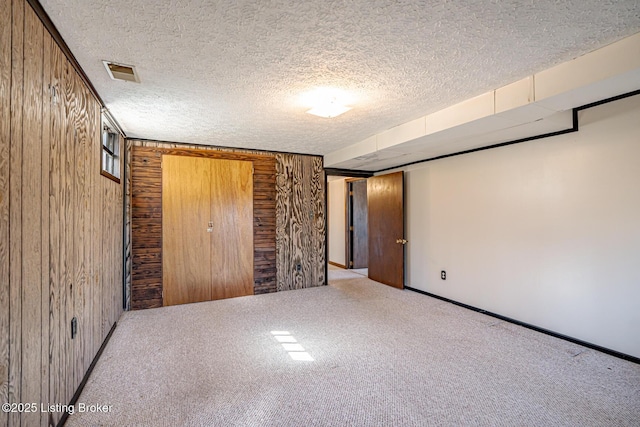 unfurnished bedroom featuring carpet, wood walls, visible vents, baseboards, and a textured ceiling