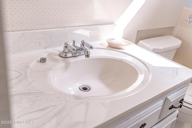 room details with wallpapered walls, vanity, and toilet