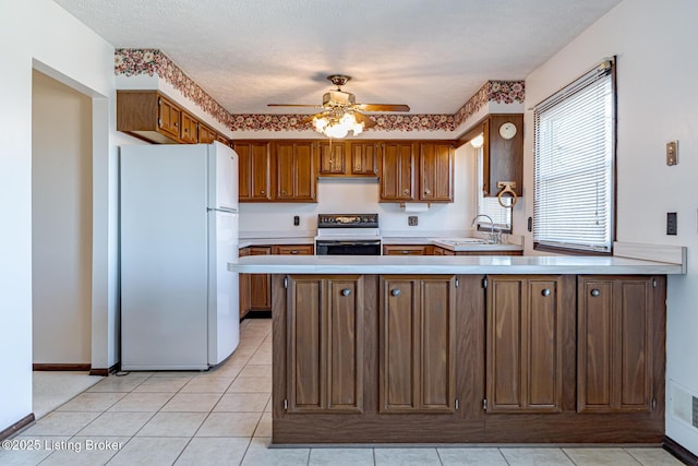 kitchen with stove, light countertops, a sink, freestanding refrigerator, and a peninsula