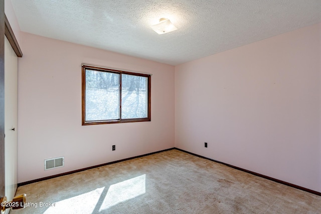 unfurnished room with light carpet, a textured ceiling, visible vents, and baseboards