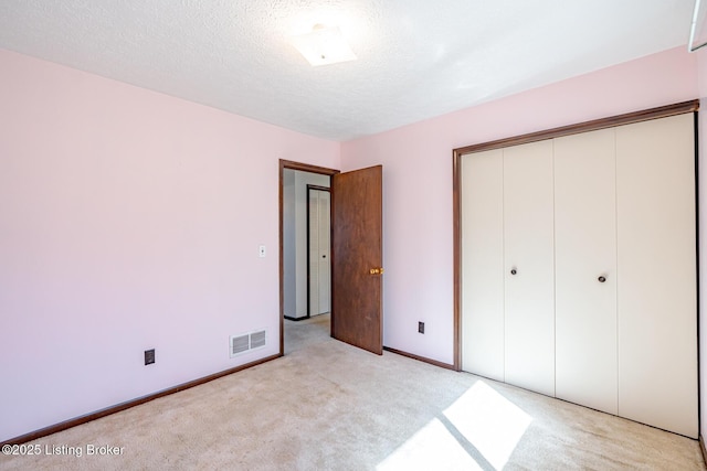 unfurnished bedroom featuring a textured ceiling, baseboards, visible vents, light colored carpet, and a closet